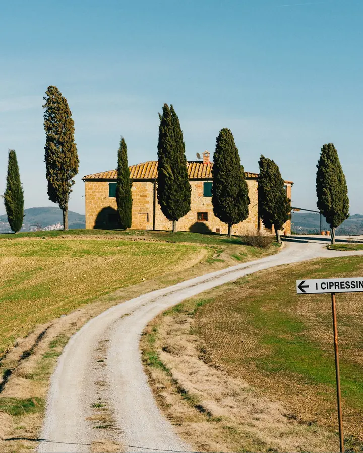 Camino de tierra entre cipreses hacia un caserío toscano